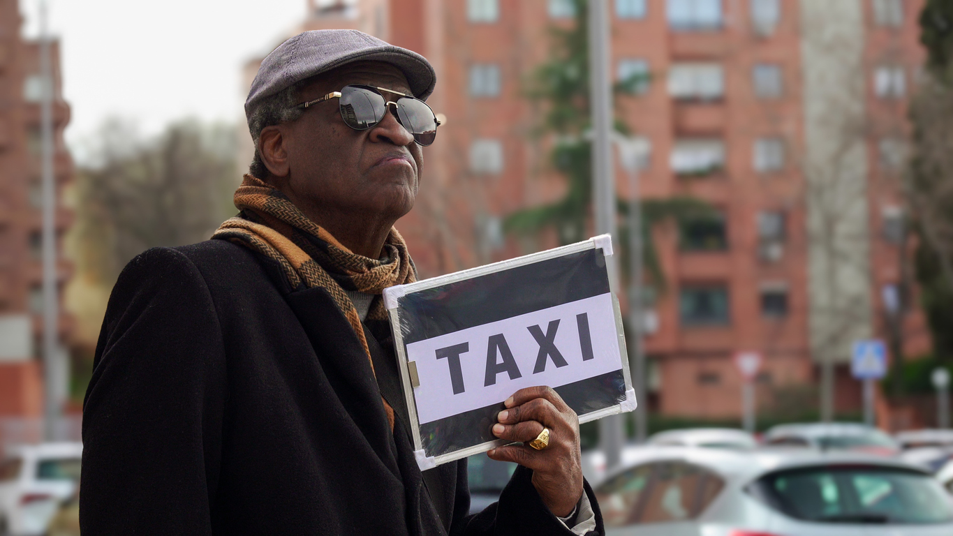 Blind person hailing a taxi using a sign with the word taxi on it.