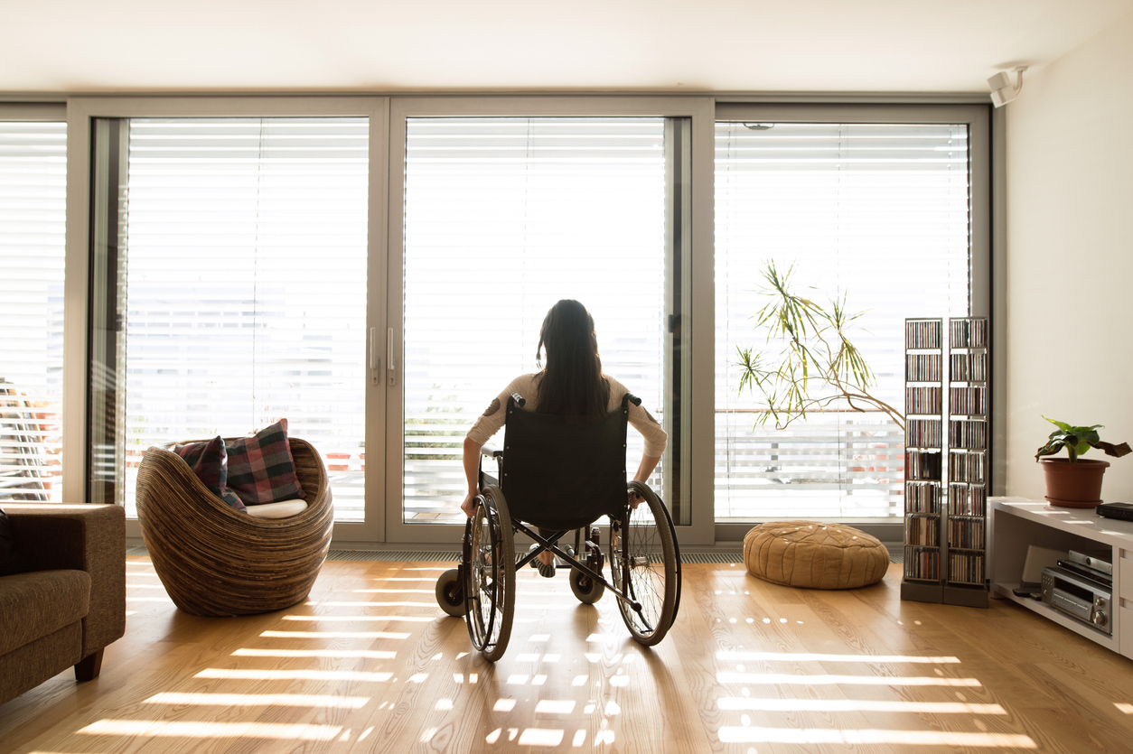 A woman sitting in a wheelchair looking out her apartment window.