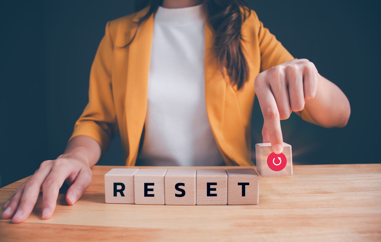 A woman sitting at a table with blocks that spell reset and one with a refresh icon it.