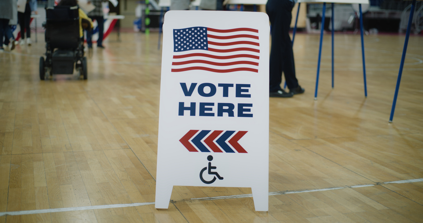 A vote here sign in a gymnasium that is serving as a polling place.